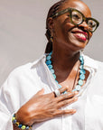 Close up shot of model wearing white shirt with blue necklace and ceramic accessories.