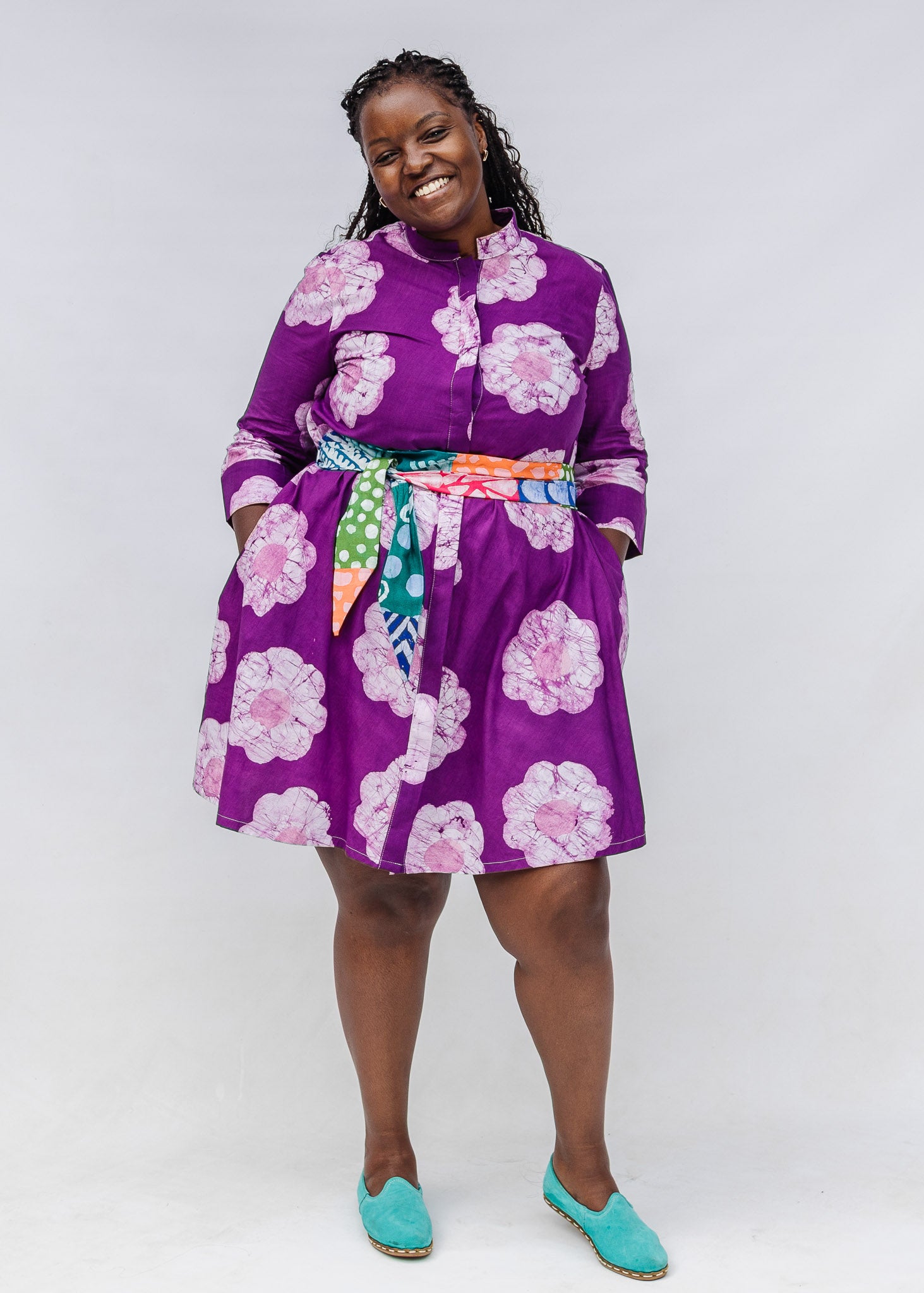 Woman wearing a purple floral dress with a colorful belt that is sold separately on a white background