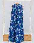 Blue sleeveless dress with white and green patterns on a wooden rack against a white background