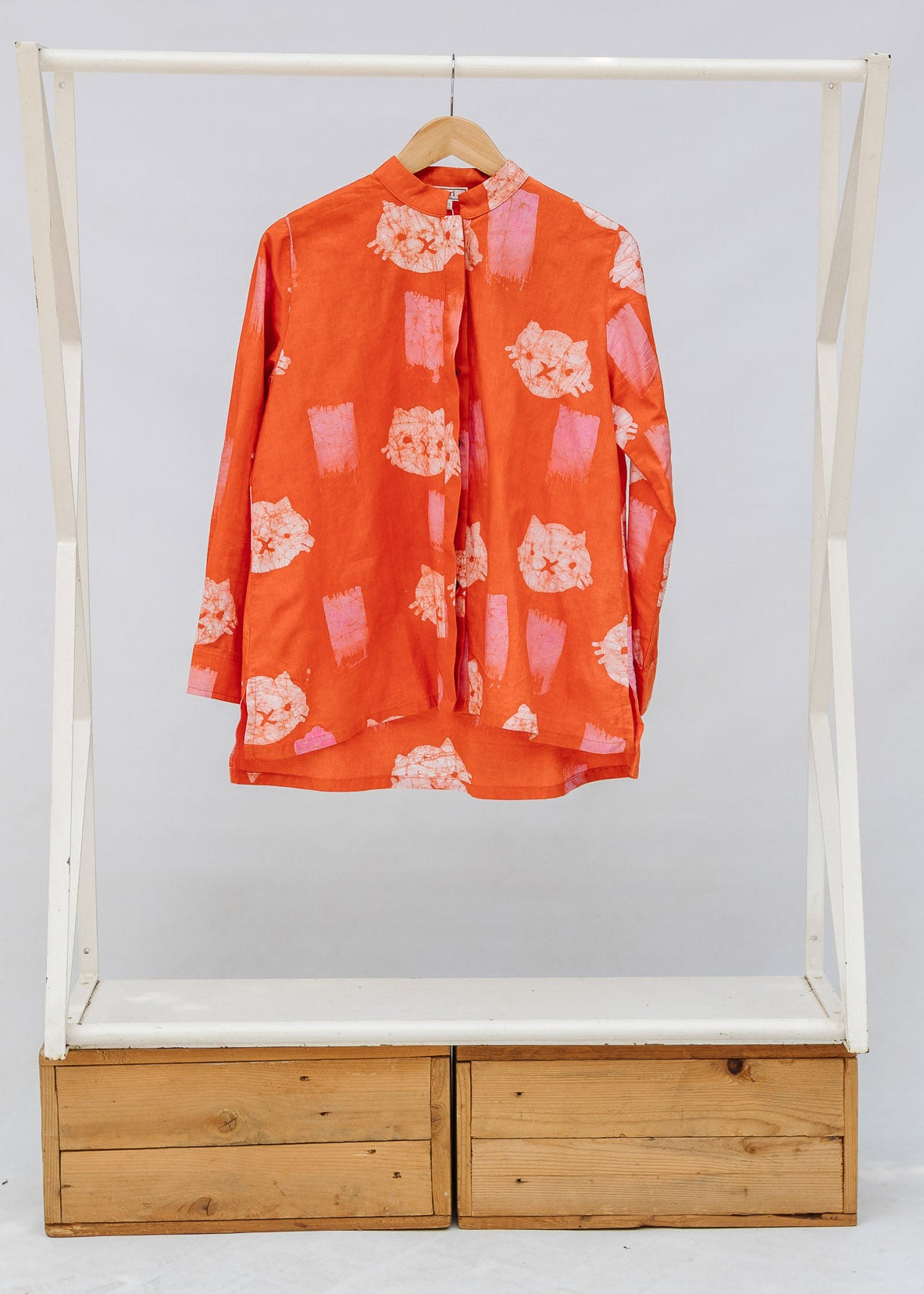 Orange shirt on a wooden and white rack with drawers against a white background