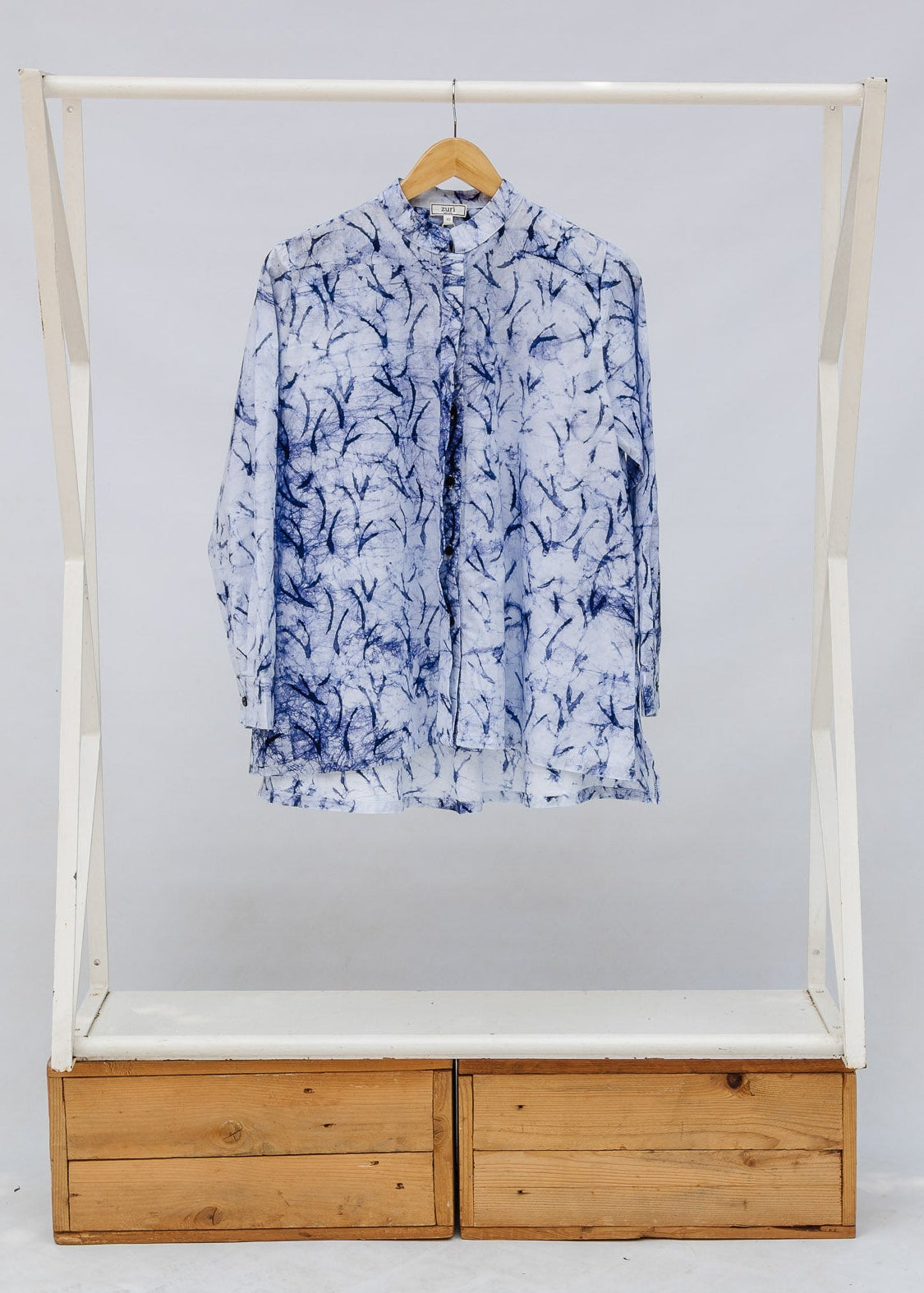 Blue and white shirt on a hanger inside a white display case with wooden base.