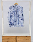 Blue and white shirt on a hanger inside a white display case with wooden base.