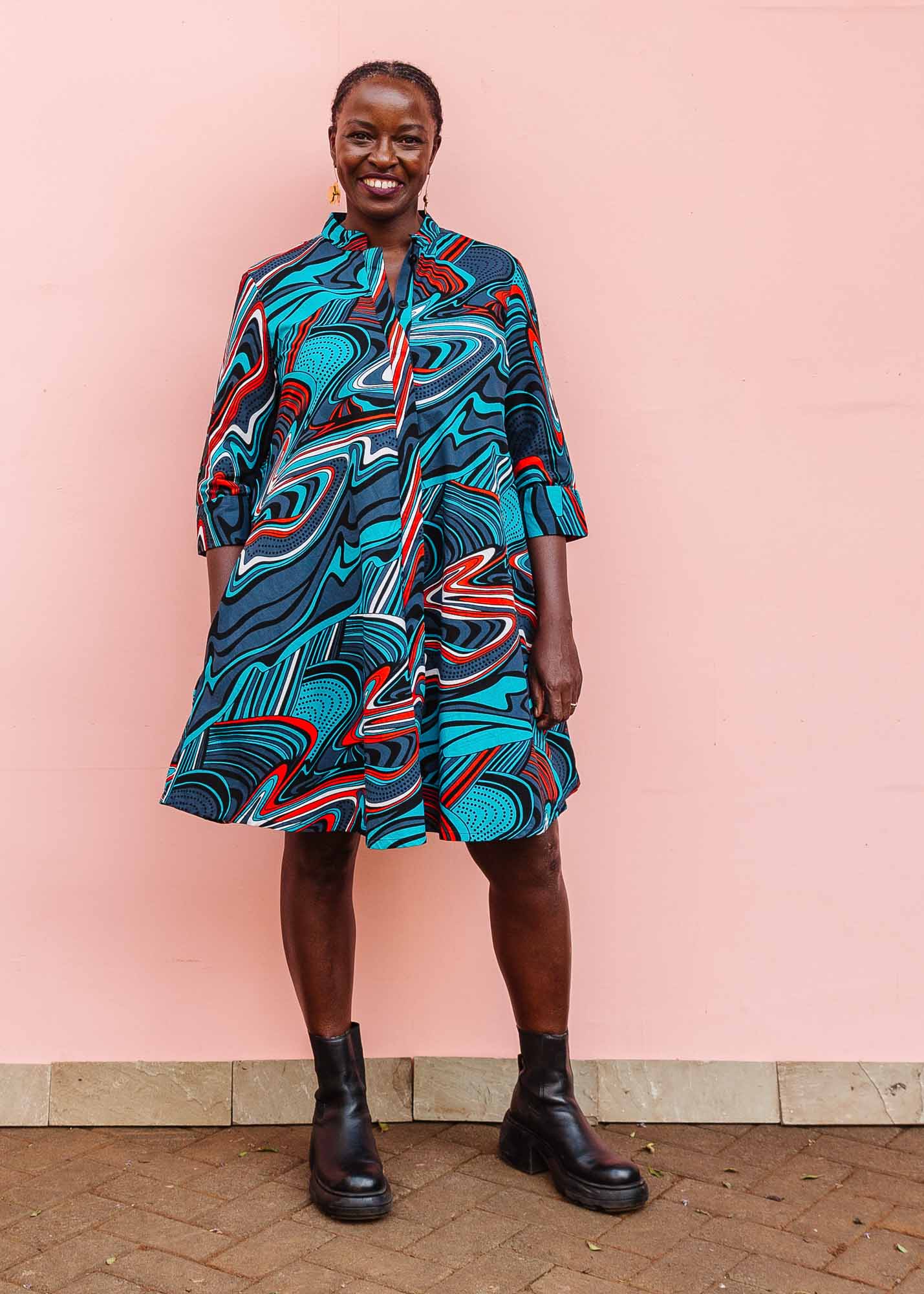 The model is wearing turquoise, black, slate, white and red abstract print dress