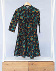 Display of black dress with teal and orange leaves with white dots.