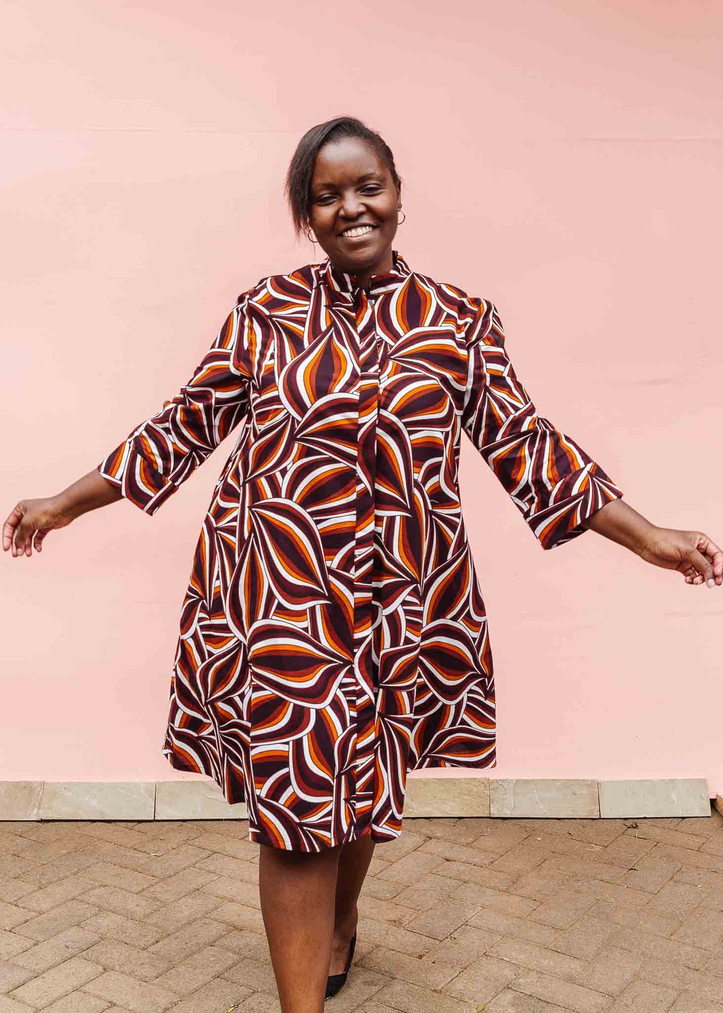 Model wearing brown, orange, burgundy and white abstract print dress.
