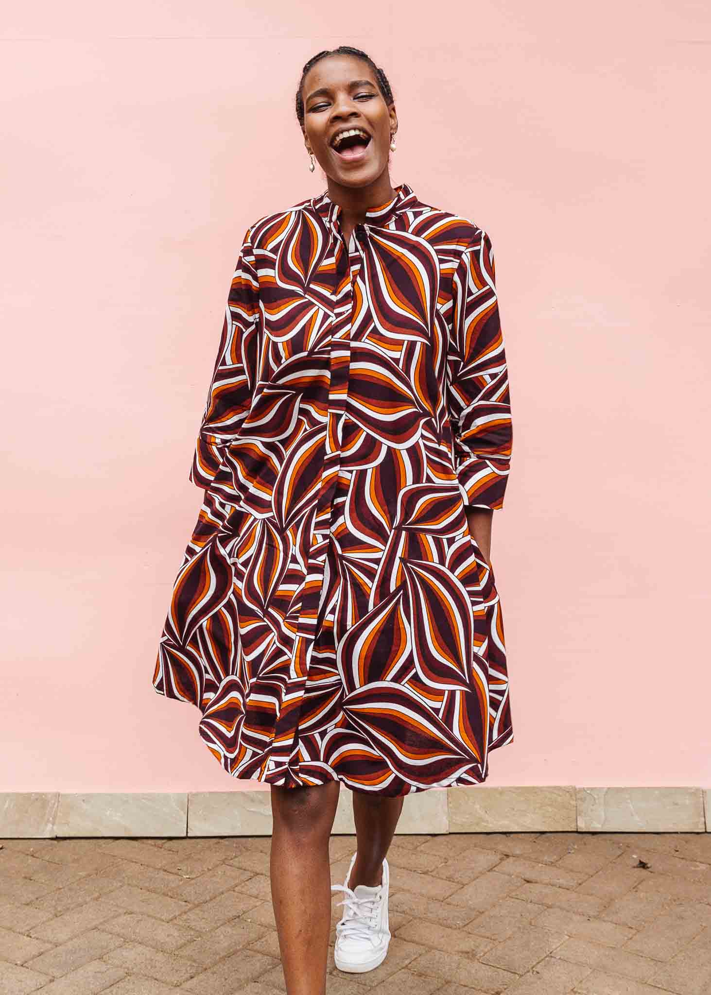 Model wearing brown, orange, burgundy and white abstract print dress.