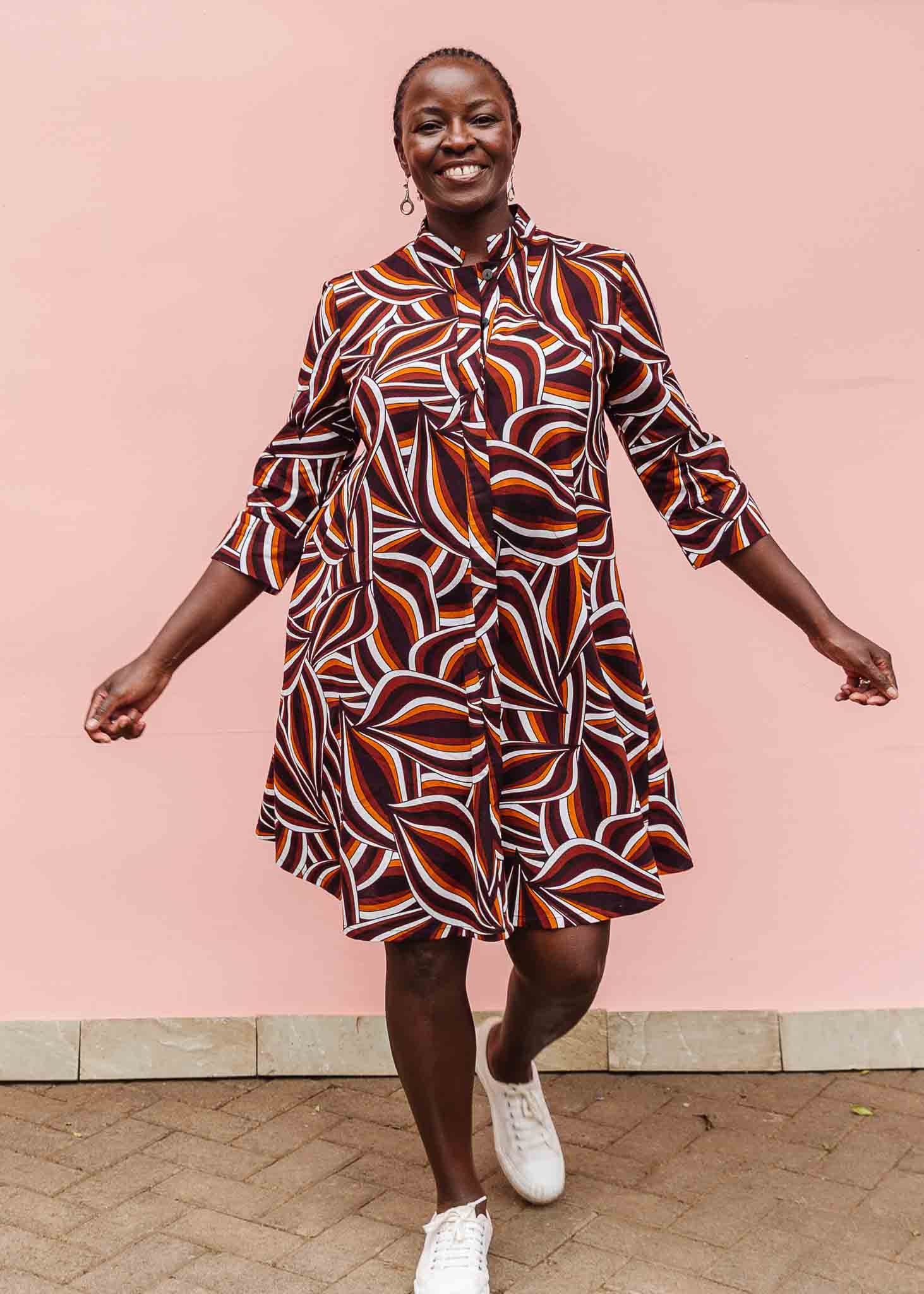 Model wearing brown, orange, burgundy and white abstract print dress.