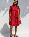 Model wearing red dress with small black and yellow branch design.