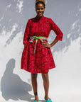 Model wearing red dress with small black and yellow branch design.