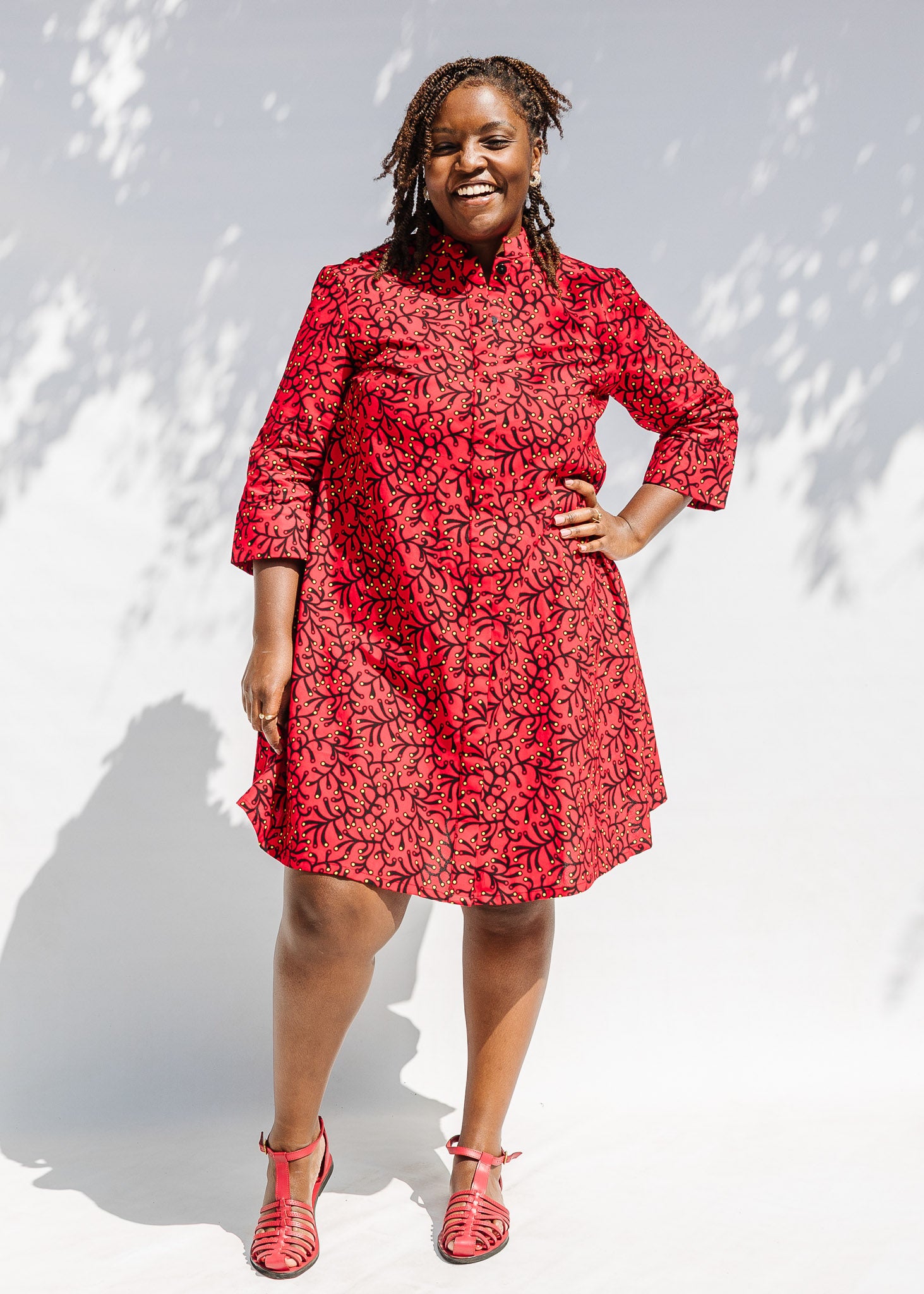 Model wearing red dress with small black and yellow branch design.