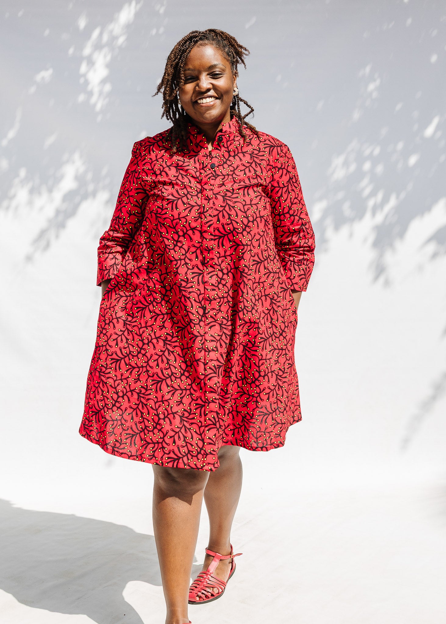 Model wearing red dress with small black and yellow branch design.