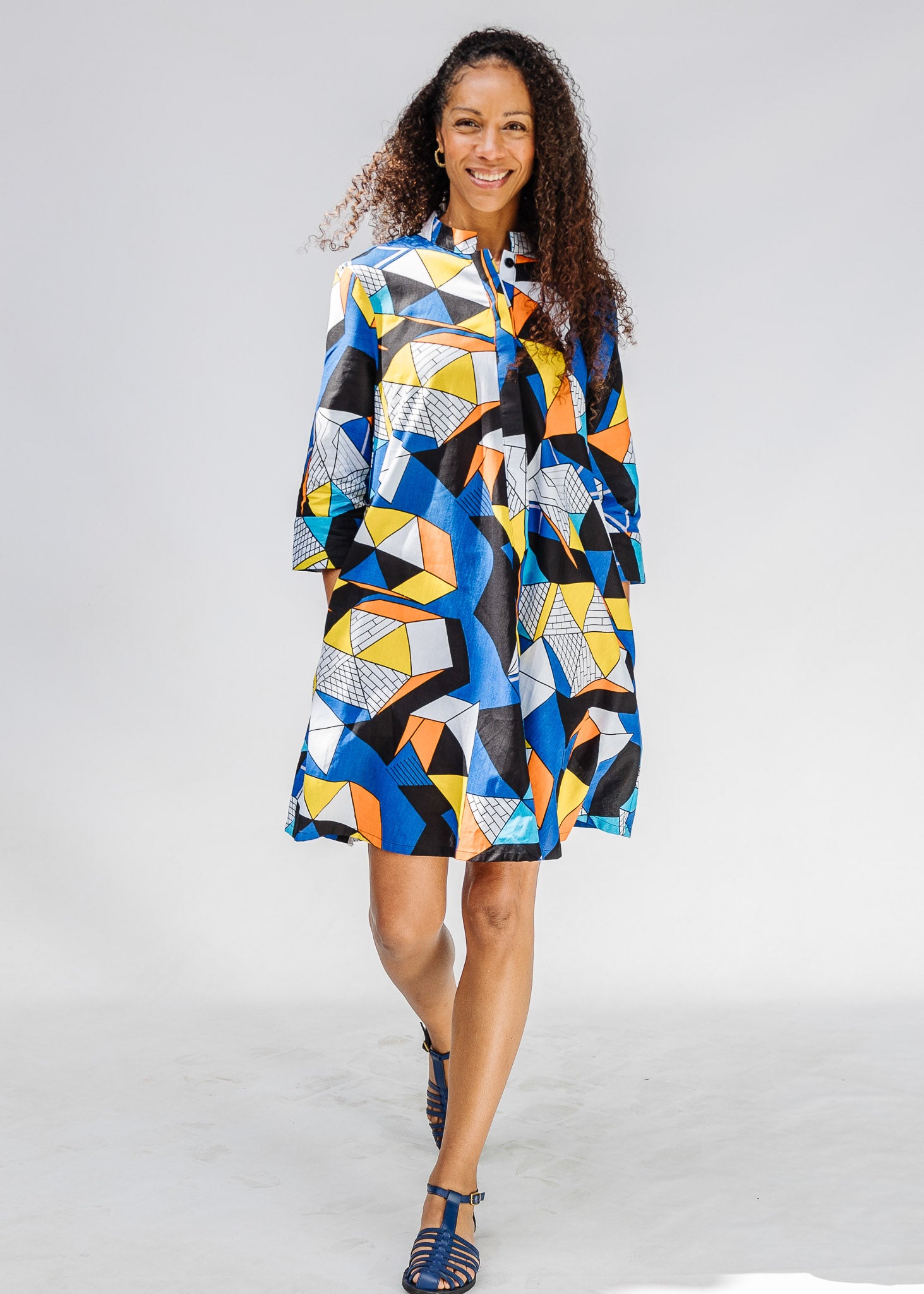 Model wearing blue dress with yellow, black, orange and white geometric print.
