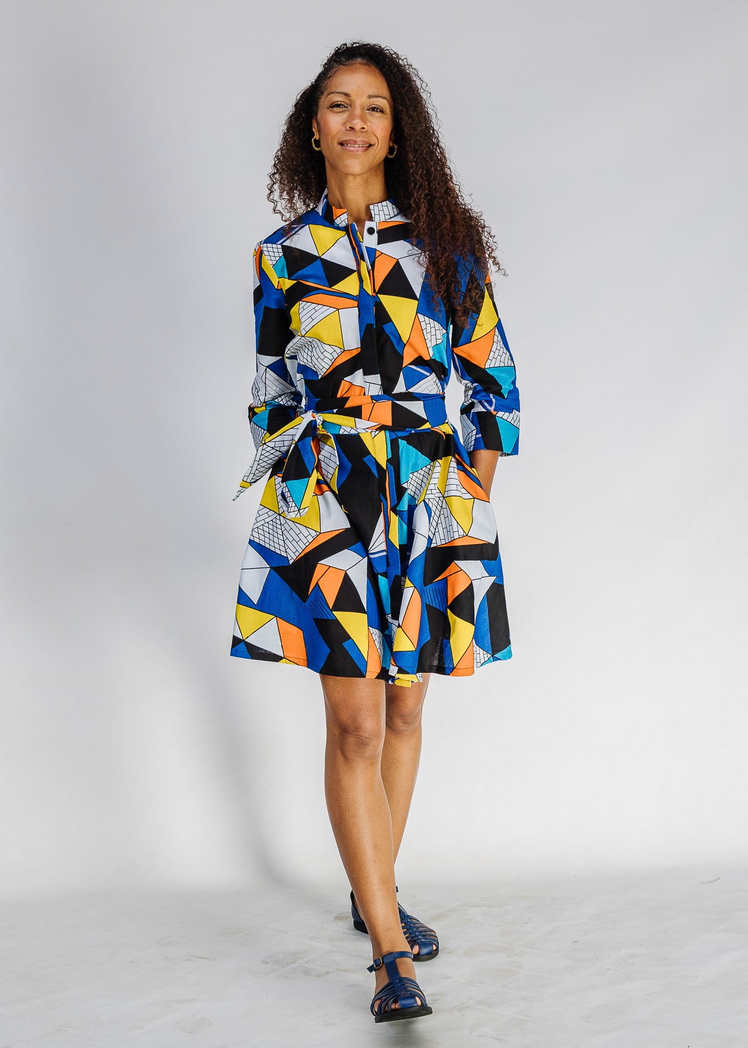 Model wearing blue dress with yellow, black, orange and white geometric print.