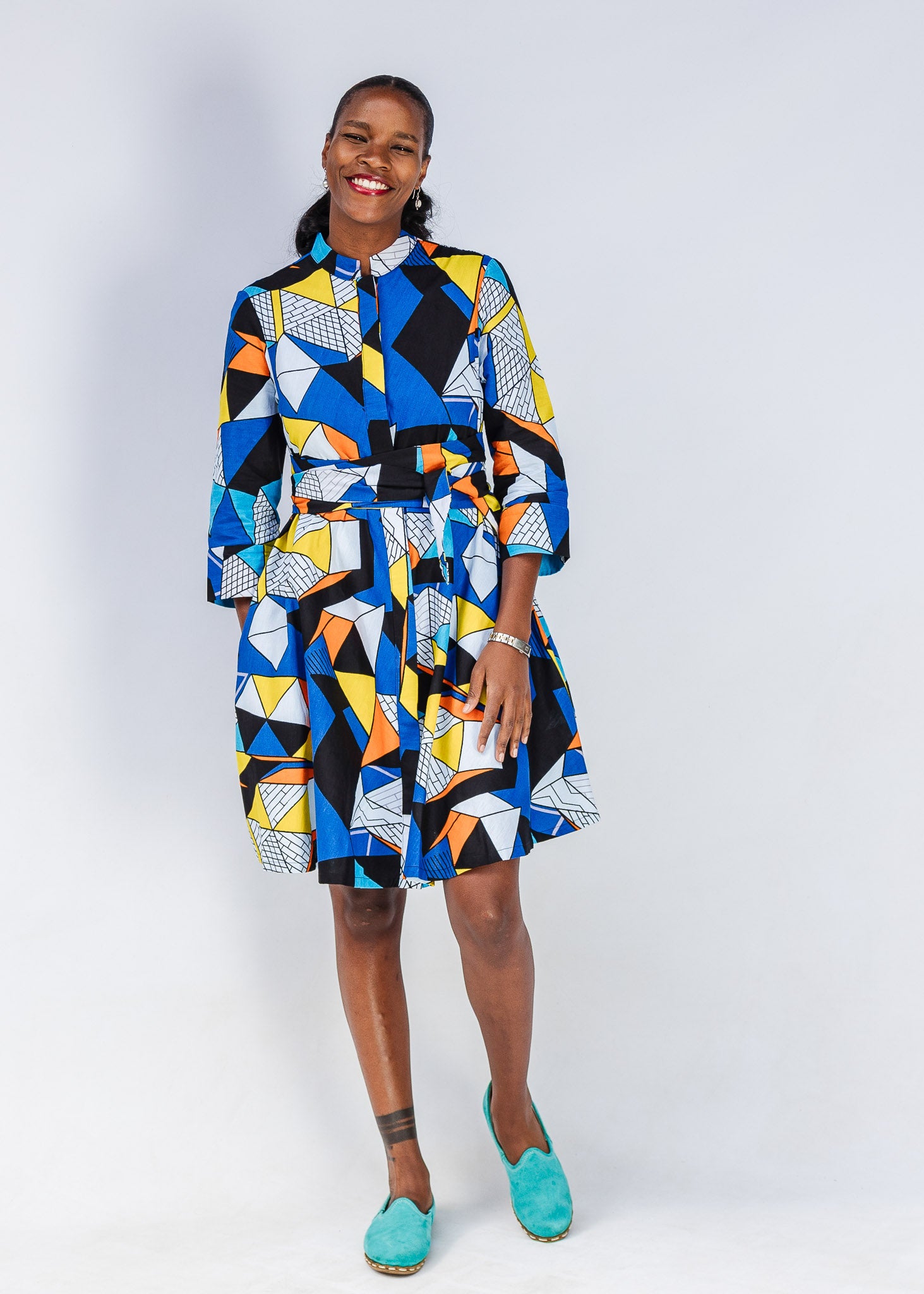 Model wearing blue dress with yellow, black, orange and white geometric print.