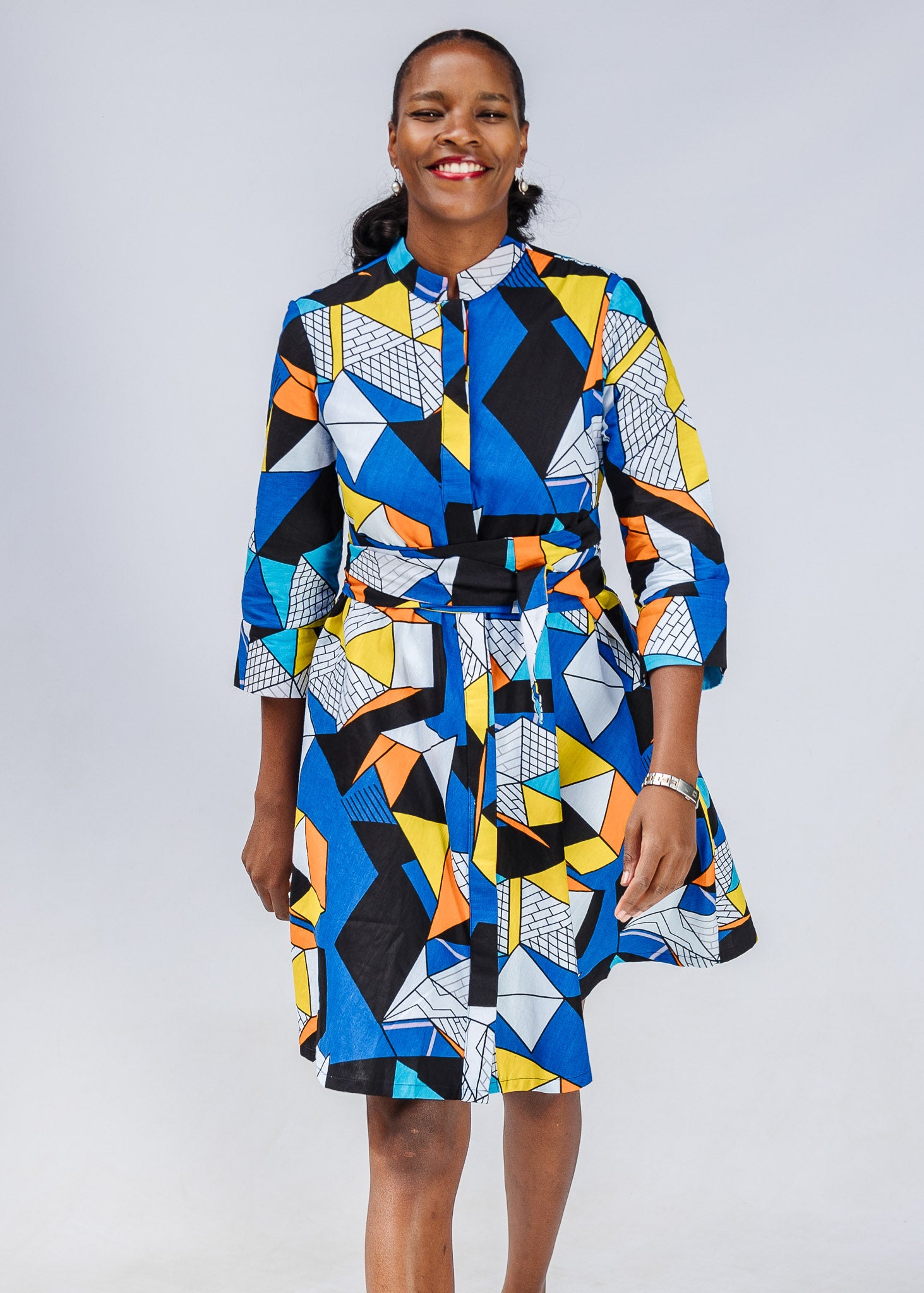 Model wearing blue dress with yellow, black, orange and white geometric print.