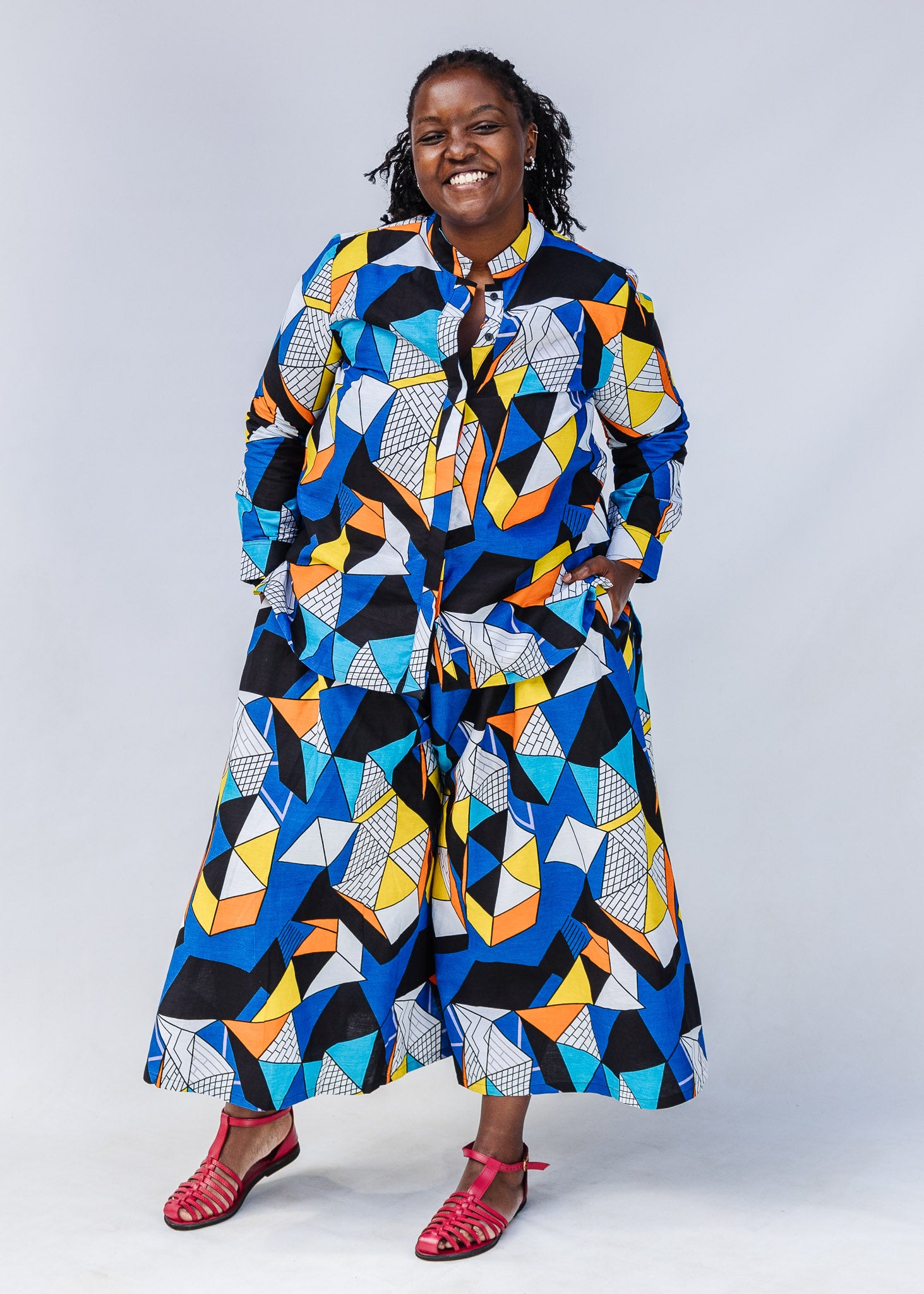 Model wearing blue, black, orange, yellow and white geometric print shirt and pant set.