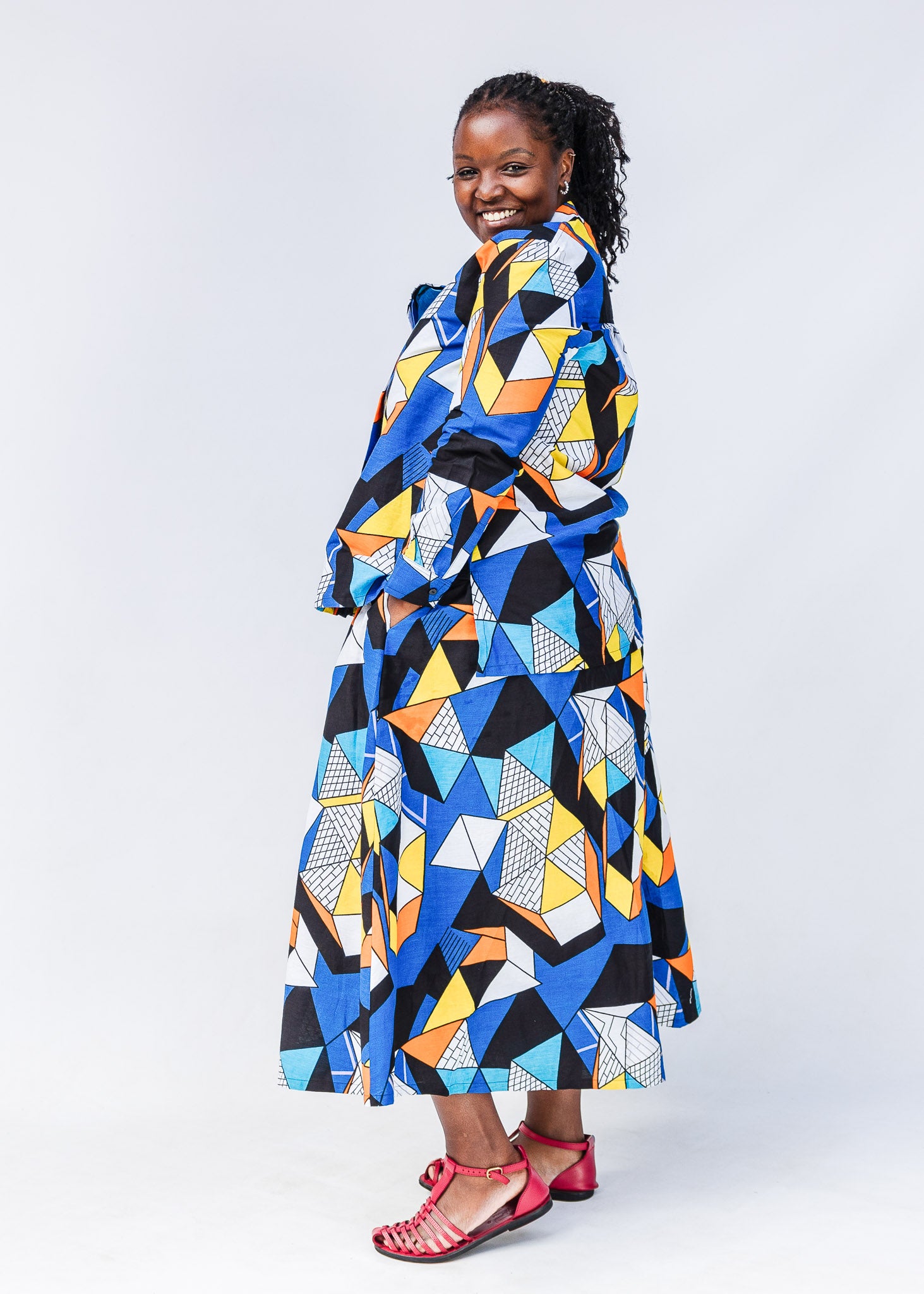 Model wearing blue, black, orange, yellow and white geometric print shirt and pant set.