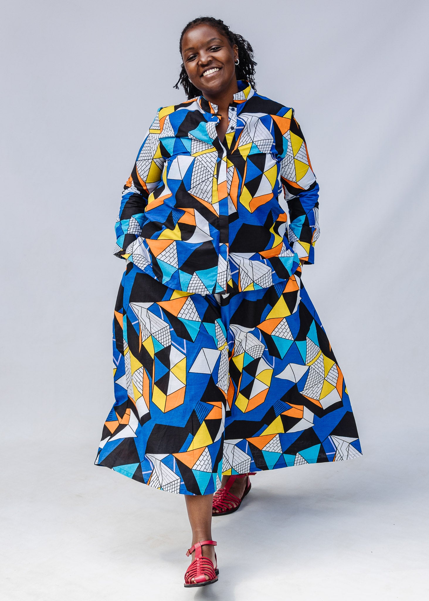 Model wearing blue, black, orange, yellow and white geometric print shirt and pant set.