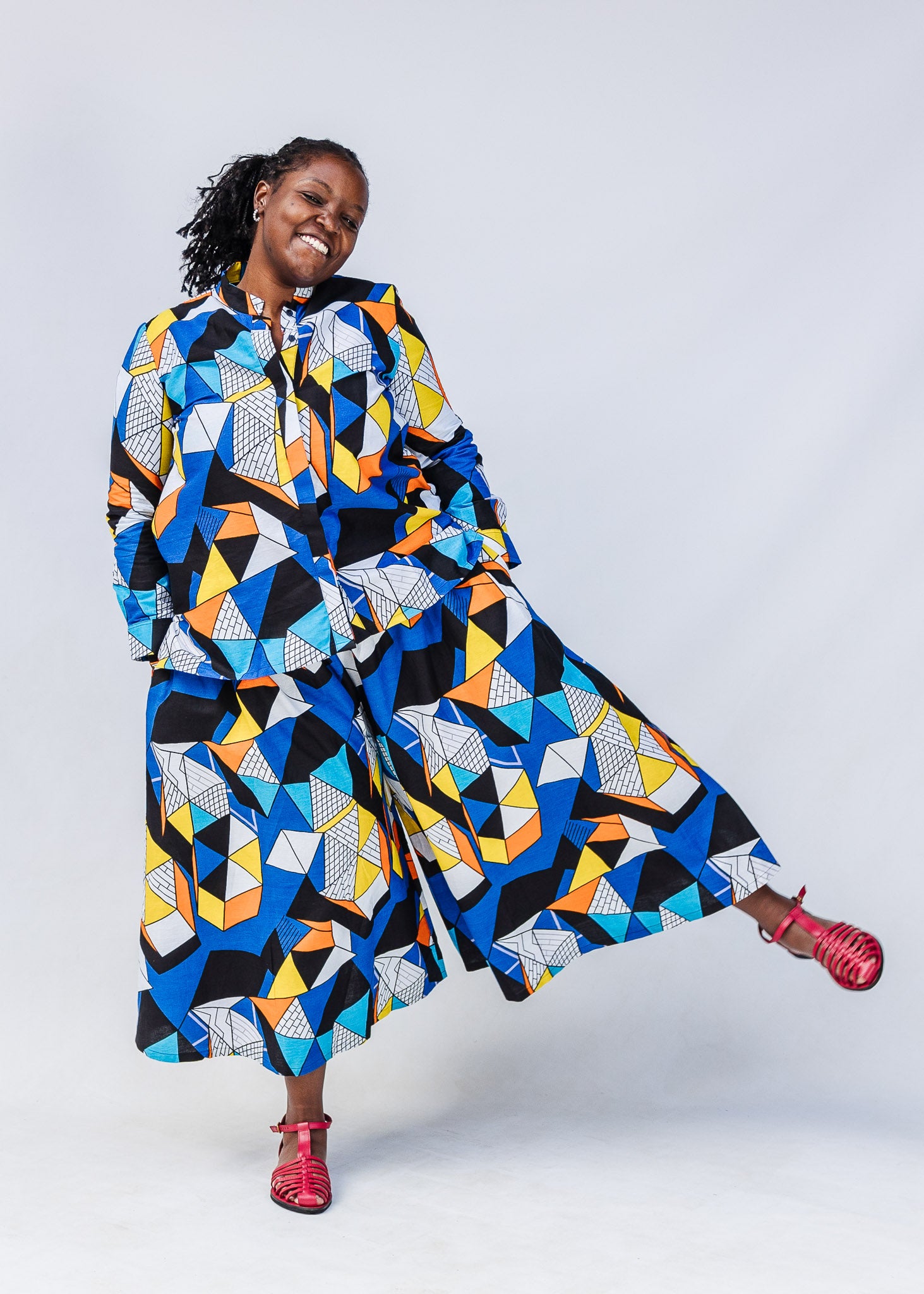 Model wearing blue, black, orange, yellow and white geometric print shirt and pant set.