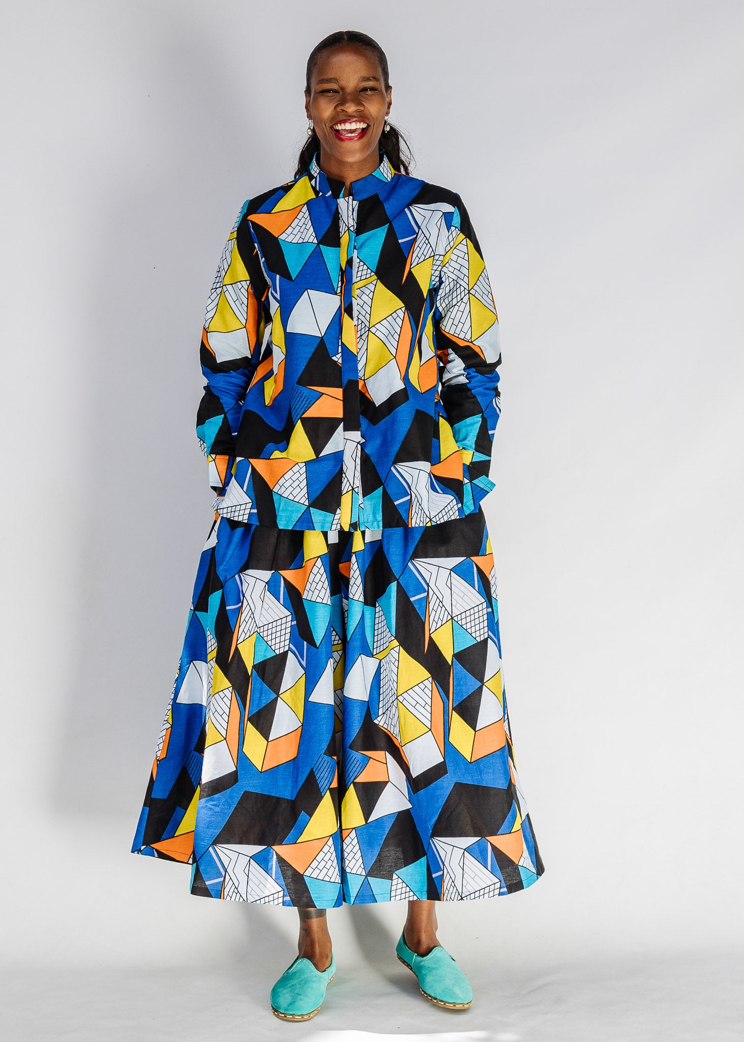 Model wearing blue, black, orange, yellow and white geometric print shirt and pant set.