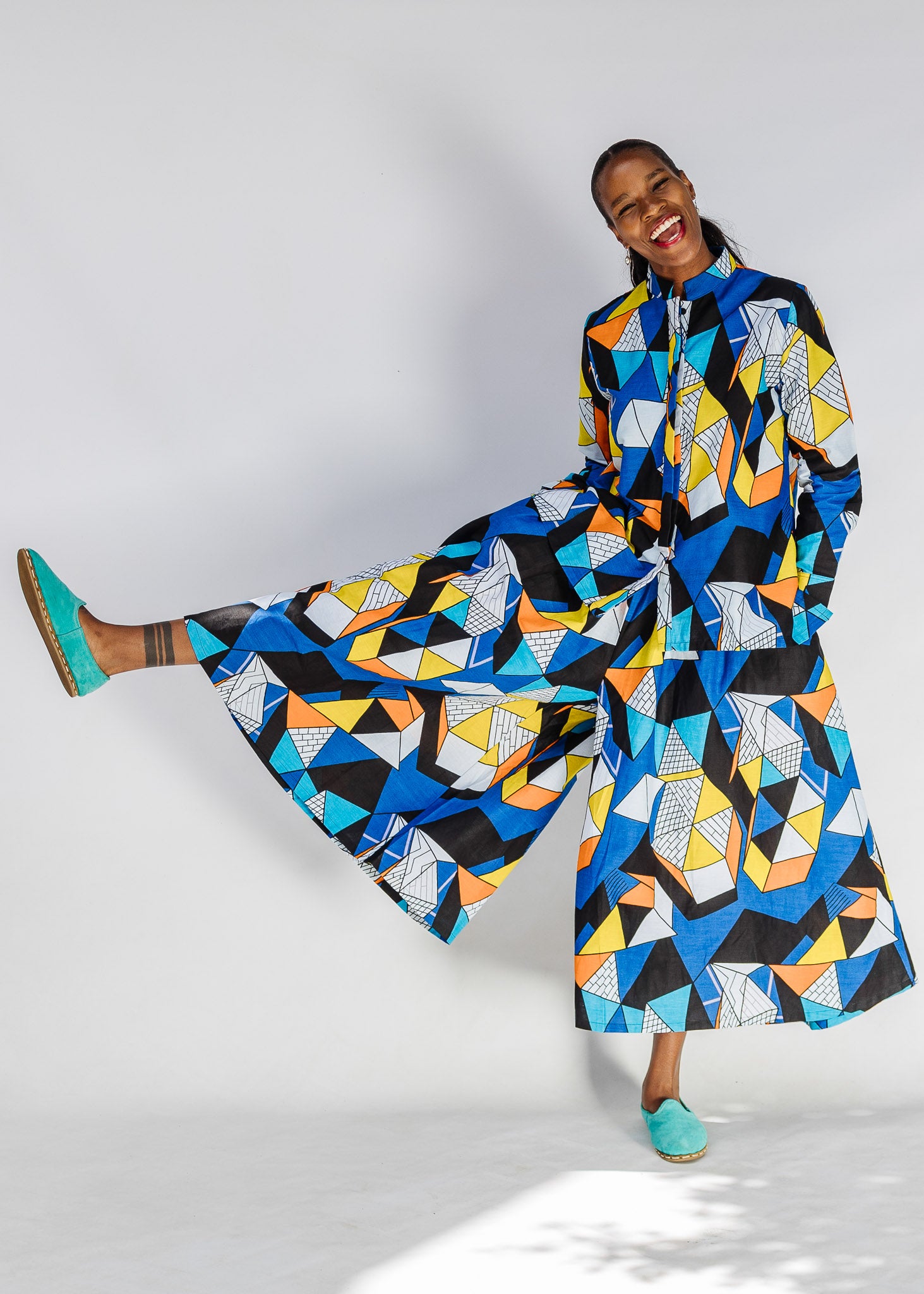 Model wearing blue, black, orange, yellow and white geometric print shirt and pant set.
