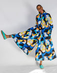 Model wearing blue, black, orange, yellow and white geometric print shirt and pant set.