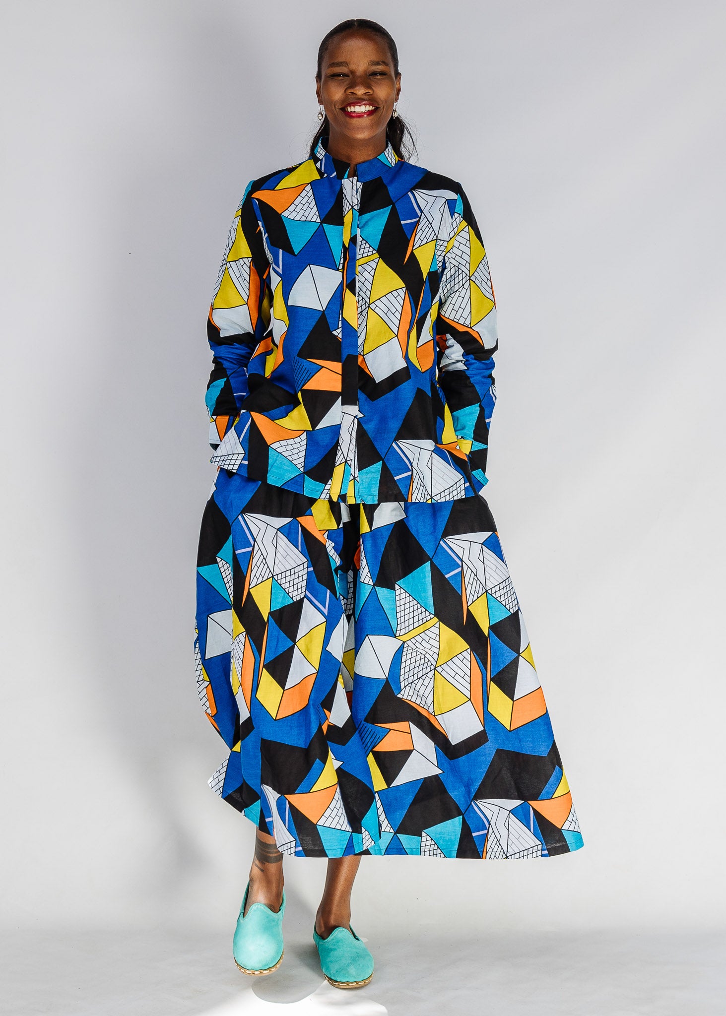 Model wearing blue, black, orange, yellow, orange and white geometric print shirt and culotte.