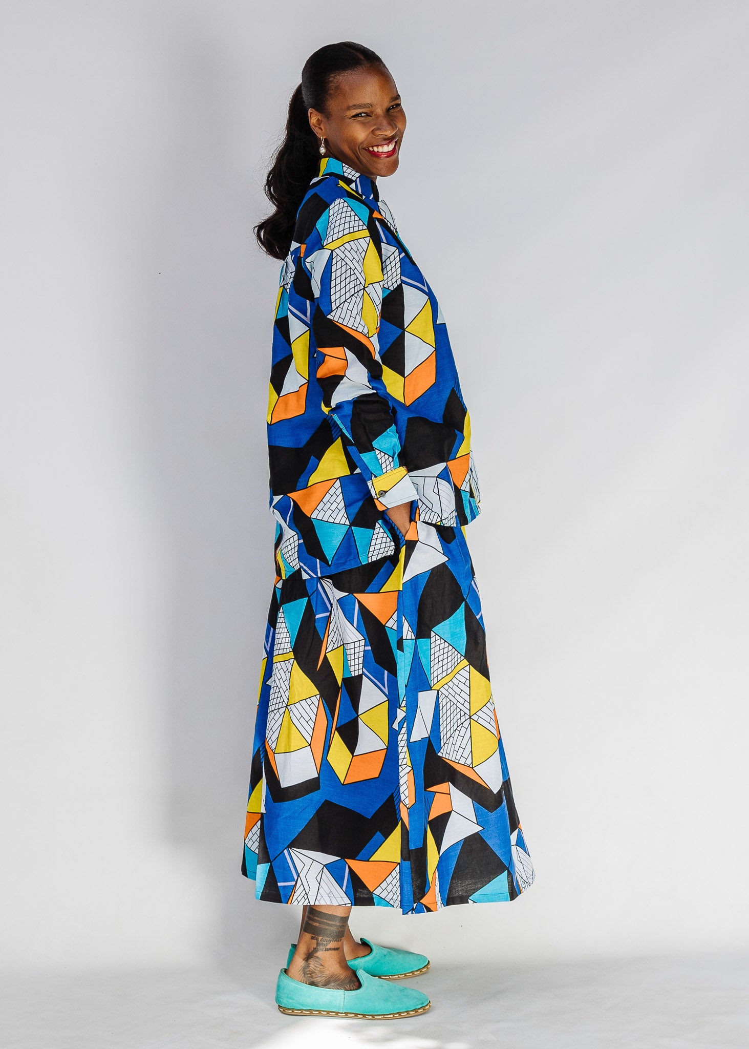 Model wearing blue, black, orange, yellow and white geometric print shirt and pant set.