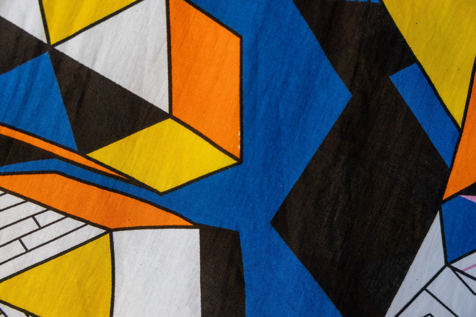Close up display of blue dress with yellow, black, orange and white geometric print, fabric.
