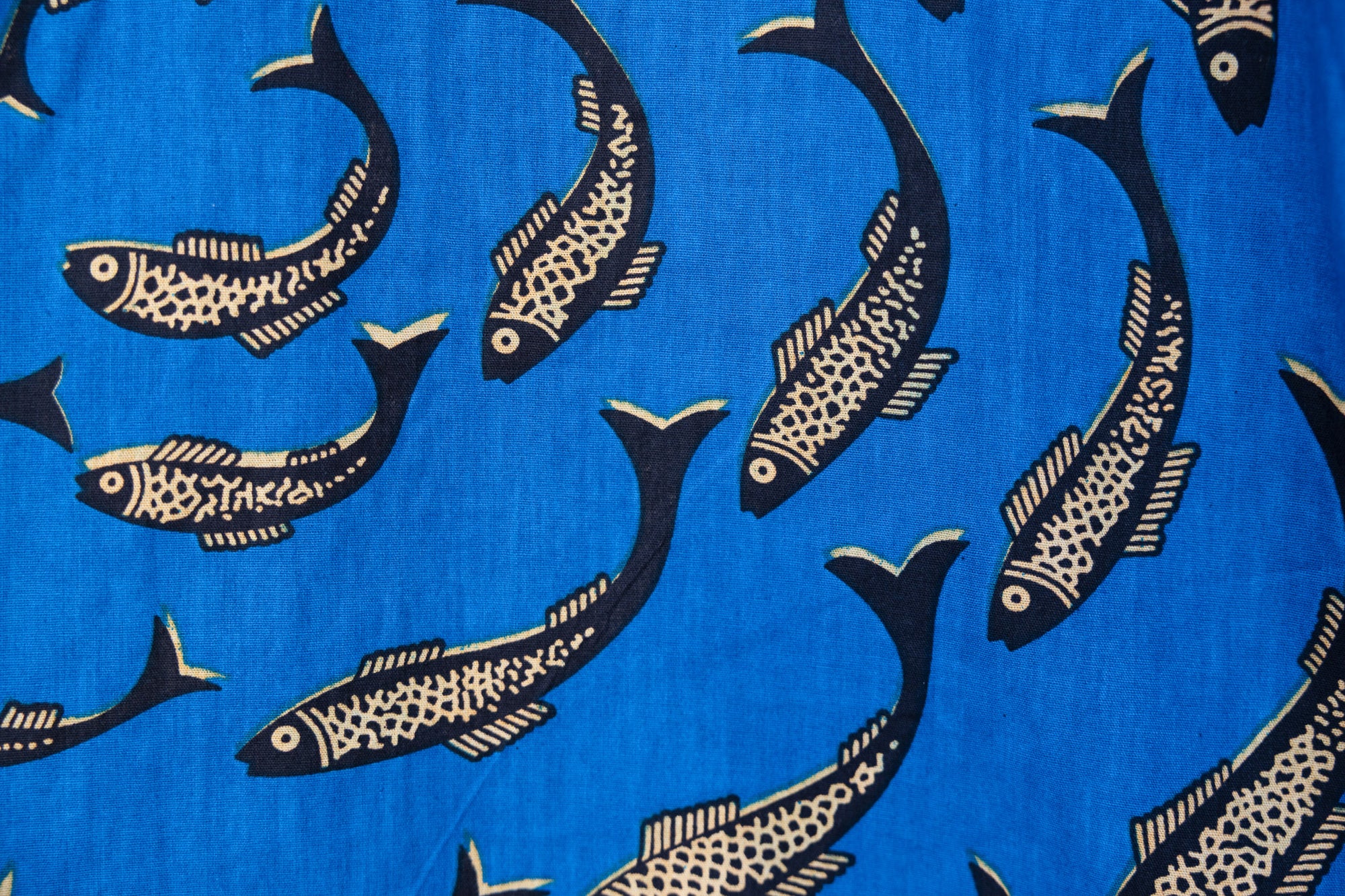 Close up display of blue dress with beige fish print, fabric.