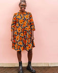 The model is wearing navy dress with orange, brown, black and white floral print