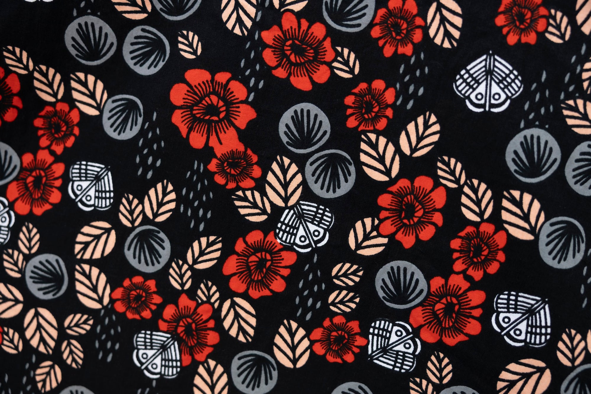 Close up display of black sleeveless shirt with red, grey and beige floral print, fabric.