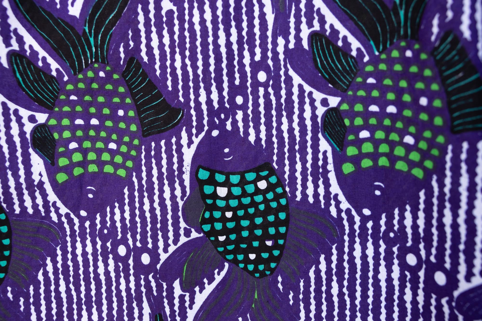 Close up display of long sleeved shirt with purple and green fish print, fabric.