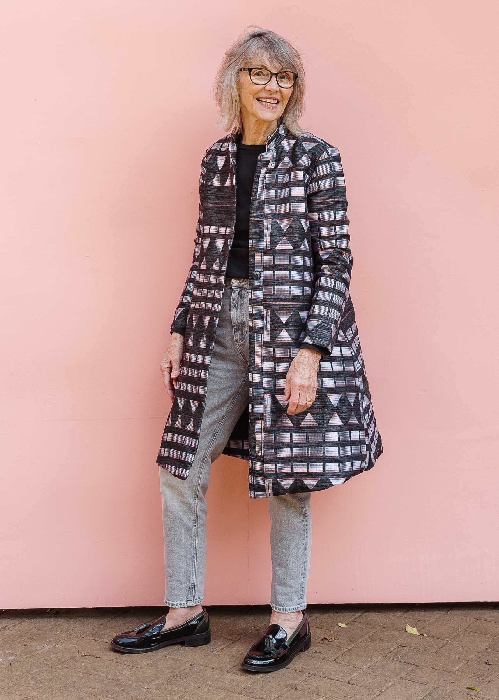 Model wearing long gray jacket with pink and white weave.