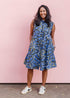 Model wearing blue sleeveless dress with green, white and navy squiggle design.
