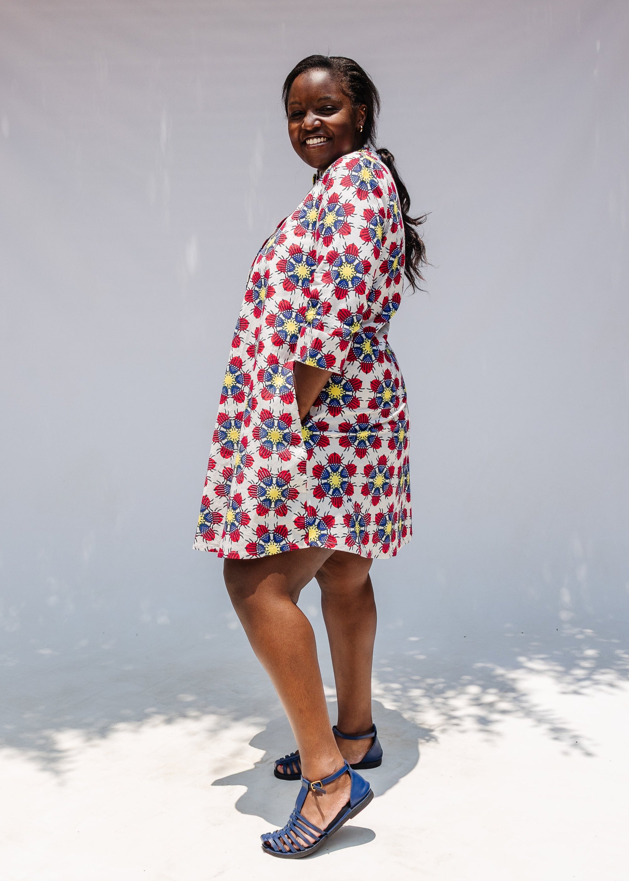 Model wearing white dress with yellow, red and blue bug print.