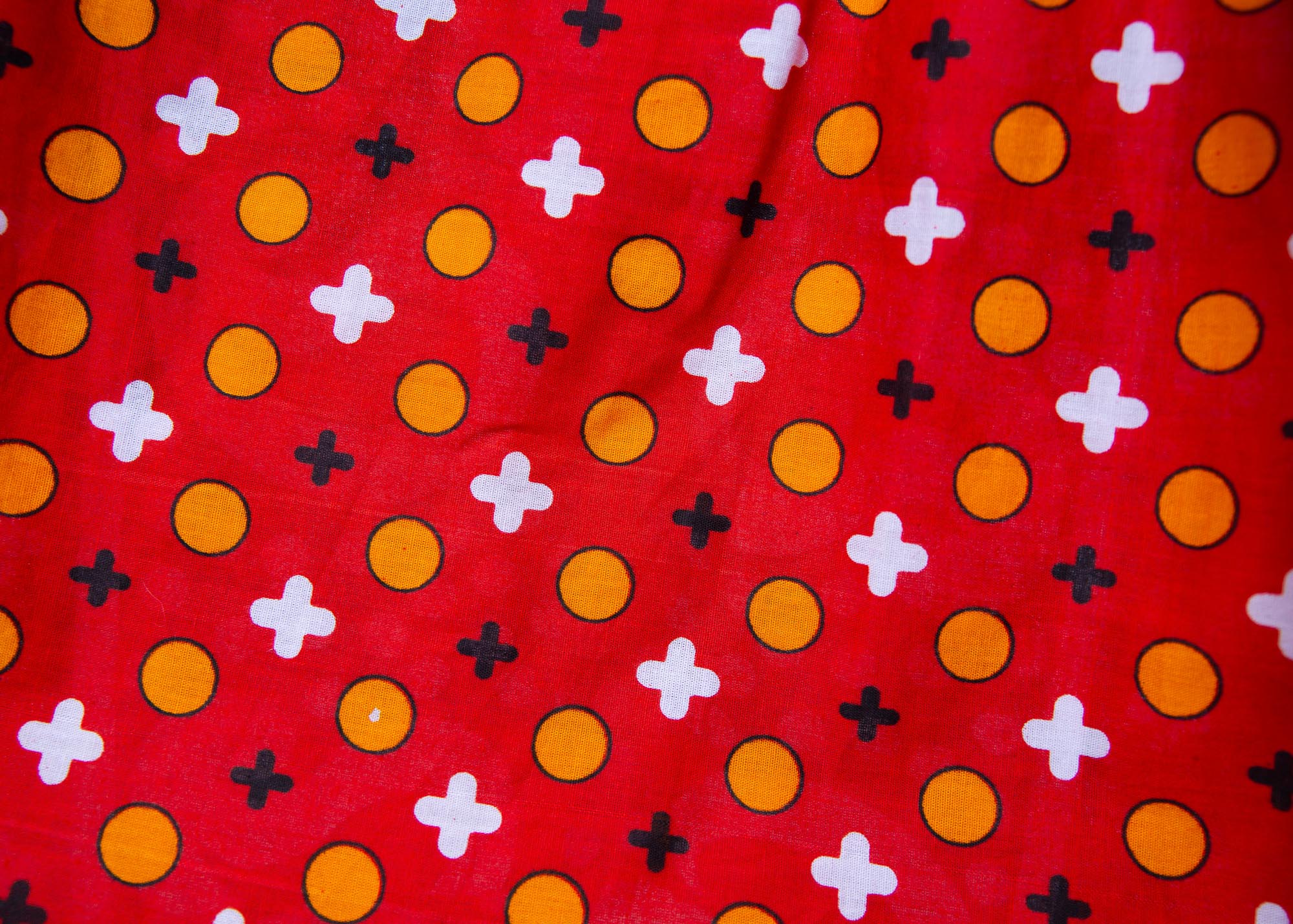 Close up display of red, white, black and orange mixed pattern long sleeved kanga shirt