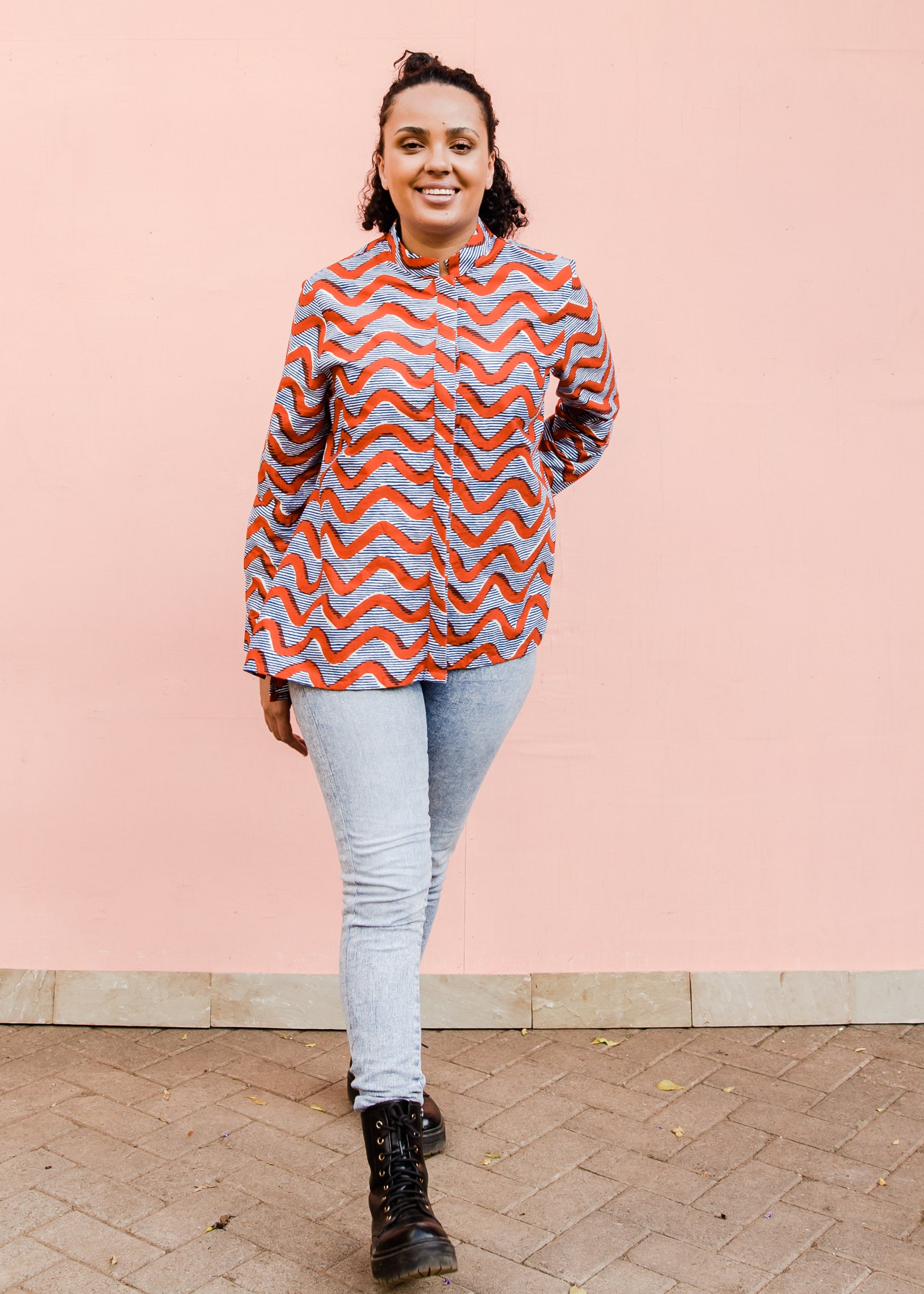 Model wearing blue and red zig zag print long sleeved blouse, paired with jeans and black boots..